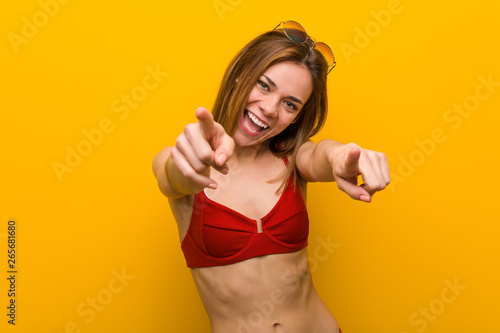 Young caucasian woman wearing bikini and sunglasses cheerful smiles pointing to front.