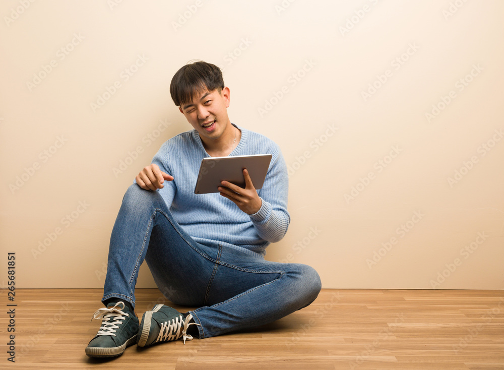 Young chinese man sitting using his tablet winking, funny, friendly and carefree gesture