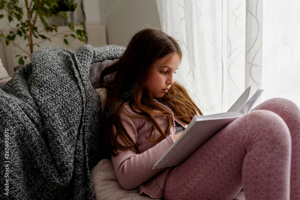 Cute little girl reading a book, at home by the window. Early reading. Cute little girl reading a book, at home by the window. Early reading.