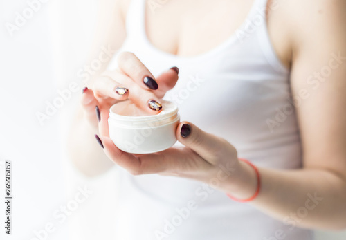 A beautiful blonde woman holds a jar of cream in her hand and applies it to her body. Skin care by moisturizing