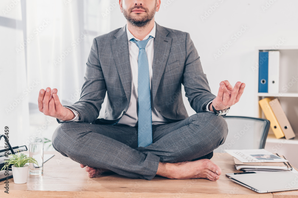 partial view of businessman meditating in Lotus Pose on office desk