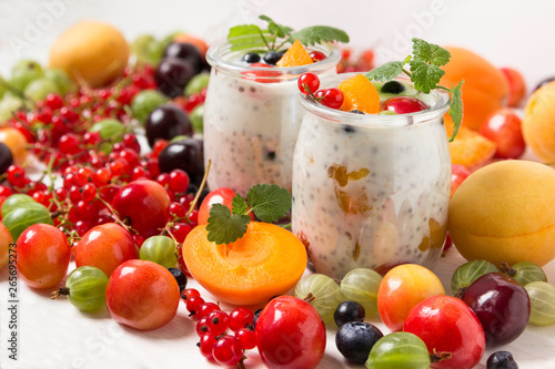 Fresh yogurt with chia seeds. Currants  cherries  gooseberries  apricots and blueberries on a white table.