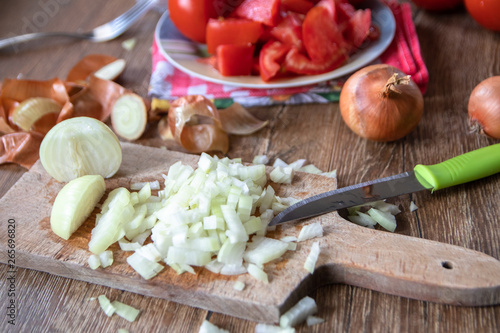 Sliced onion on kitchen board, whole onion and tomatoes in the background. Old wooden table.