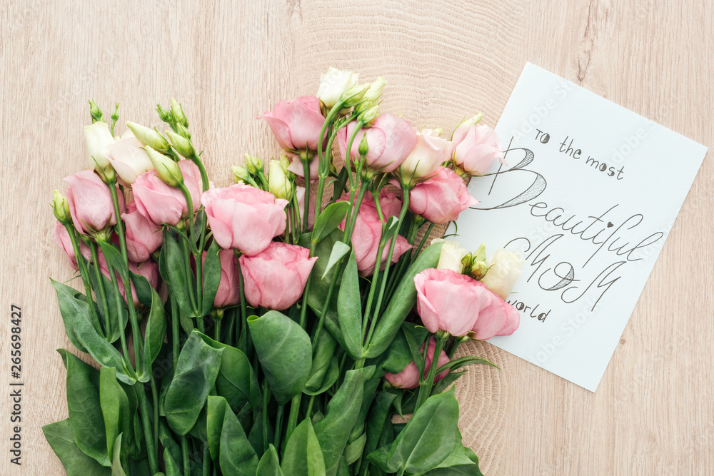 Fototapeta premium top view of pink eustoma flowers and card with to the most beautiful mom in the world lettering on wooden table