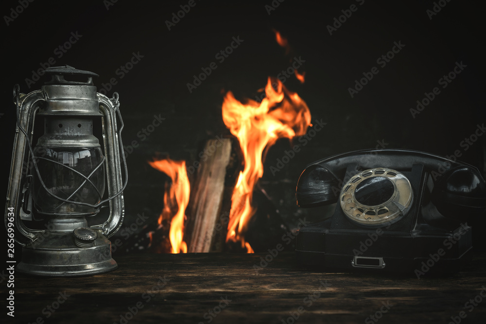 Black old phone and kerosene lamp on a table on a burning fire in fireplace  background. Stock Photo | Adobe Stock