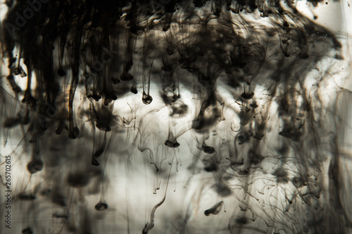 a cloud of ink in a transparent glass cup with clear water against the backdrop of a striped screen with rays of light. Template, layout, background, texture. macro diffusion black and white