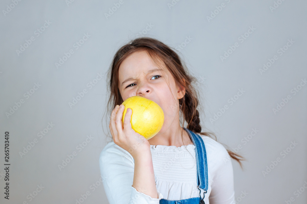 Emotional portrait little beautiful girl with pigtails in jeans overalls eating bites holding an apple. 6-7 years studio Emotional portrait little beautiful girl with pigtails in jeans overalls eating bites holding an apple. 6-7 years studio