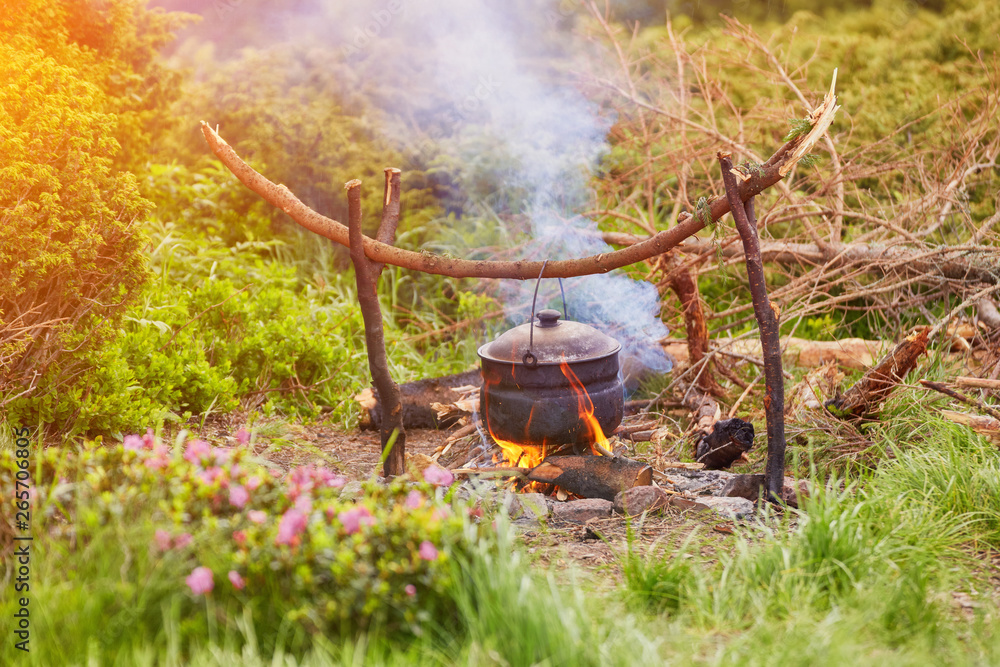 Old small kettle is heated on a bonfire on a green mountain meadow during a bad weather. Old small kettle is heated on a bonfire on a green mountain meadow during a bad weather.