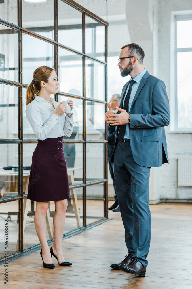 handsome bearded businessman looking at businesswoman holding cup of coffee in office handsome bearded businessman looking at businesswoman holding cup of coffee in office