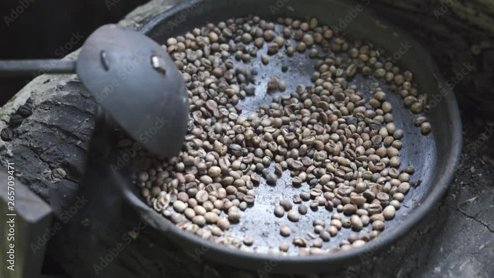 Coffee beans being roasted using a traditional method in a metal dish ...