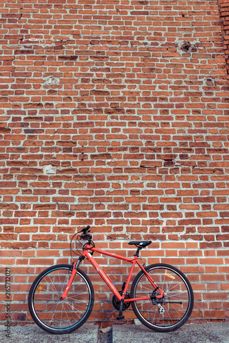 Red bicycle on the background of a brick old wall. Free space for text. The concept of parking and abandoned bike. Locked and parked, locking cable on the frame of the bike. In summer in the city.