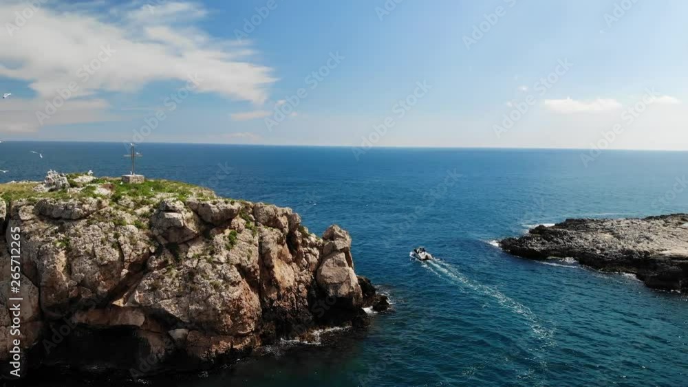 Aerial parallax revealing a beautiful rocky island with a cross monument on the top and seagulls flying around Aerial parallax revealing a beautiful rocky island with a cross monument on the top and seagulls flying around