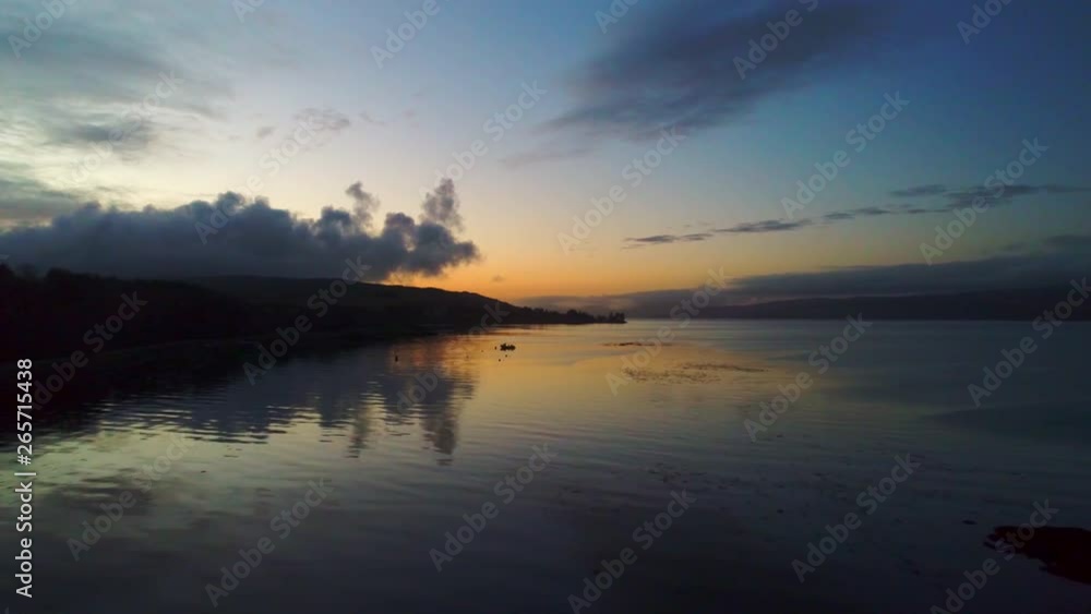 Drone moving backwards over calm water at sunset near the coastline of Salen on the Isle of Mull Drone moving backwards over calm water at sunset near the coastline of Salen on the Isle of Mull