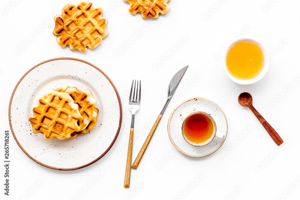 Breakfast with Belgian waffles with honey, tea, knife, fork and spoon on white background top view Breakfast with Belgian waffles with honey, tea, knife, fork and spoon on white background top view