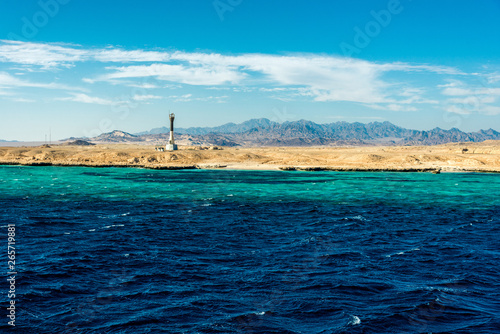 Seascape, high lighthouse against the blue sea with high bald mountains in the background © Алексей Еремеев