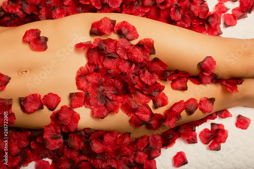 Caucasian woman's hips, thighs, and stomach covered by rose petals on a bed