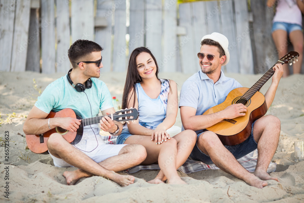 Young,happy and beautiful friends with a guitar at the beach