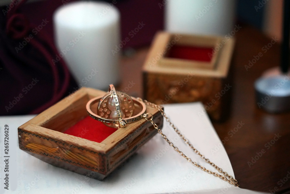 Magical golden round mascot with a chain in wooden box on the book on a blurred background. Occult, esoteric, fortune-telling and wicca concept. Mystic and vintage background. Magical golden round mascot with a chain in wooden box on the book on a blurred background. Occult, esoteric, fortune-telling and wicca concept. Mystic and vintage background.