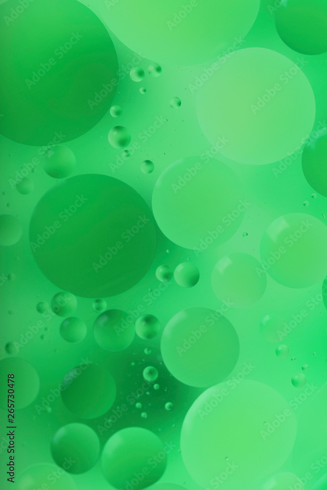Blurred abstract background. Macro shot of oily liquid. Green circles and wavy lines of different sizes. Blur, vertical, a lot of free space for text, nobody, macro. Concept of design.