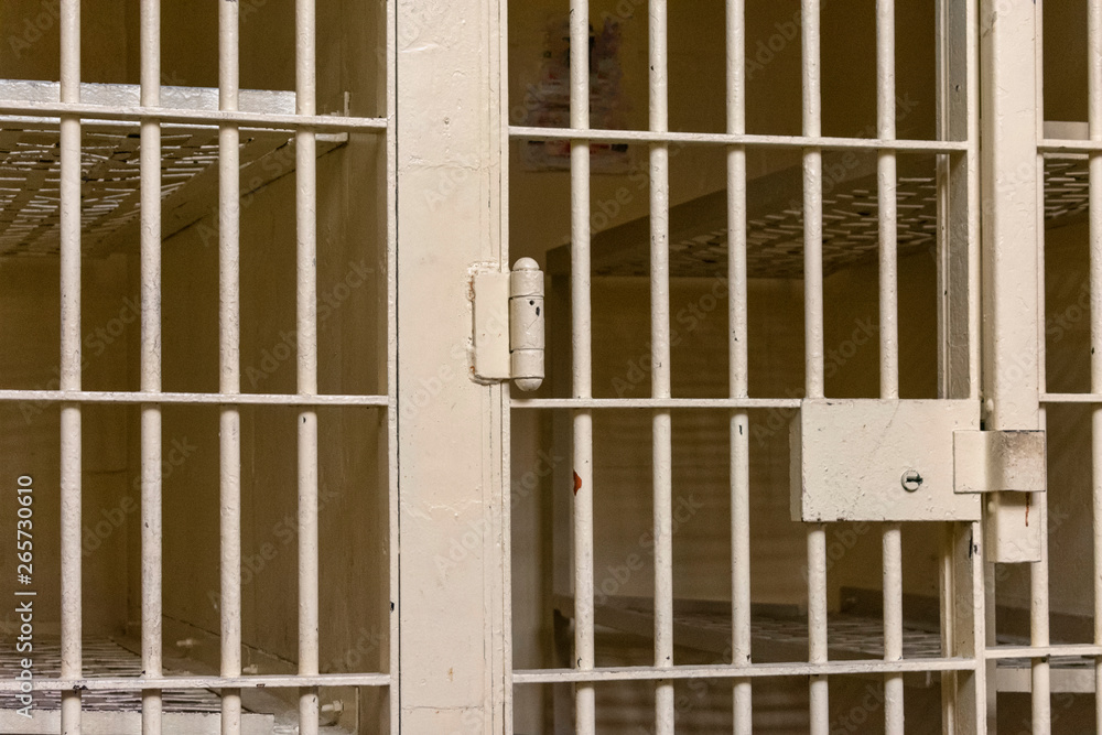 Prison cell behind the bars with no inmate. Empty jail cell with locked steel door. Prison cell behind the bars with no inmate. Empty jail cell with locked steel door.
