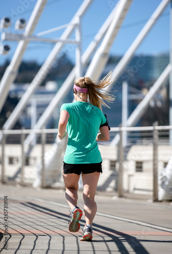 Pretty shaped girl with long hair listening music with headphones while running on the bridge photo