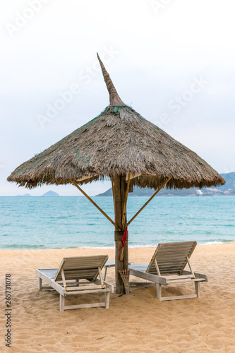 Big parasol of straw with two loungers on sandy beach for relax