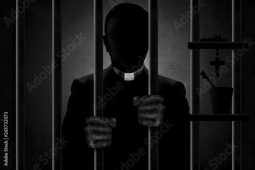 Фотография A Catholic priest identified by his clergyman collar is seen in silhouette behind bars with his filthy hands gripping the bars