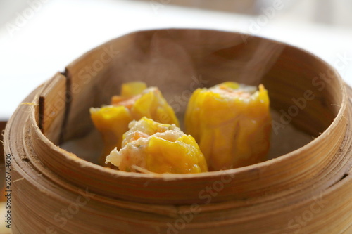 Close up hot Cantonese Shumai (Siu Mai) Dim Sum, shrimp & pork Chinese steamed dumplings recipe wrap by yellow wonton wrapper (Kanom Jeeb in Thai) in bamboo basket in dim sum set have smoke photo