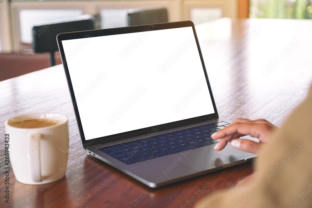 Mockup image of a woman's hand using and touching on laptop touchpad with blank white desktop screen with coffee cup on wooden table Mockup image of a woman's hand using and touching on laptop touchpad with blank white desktop screen with coffee cup on wooden table