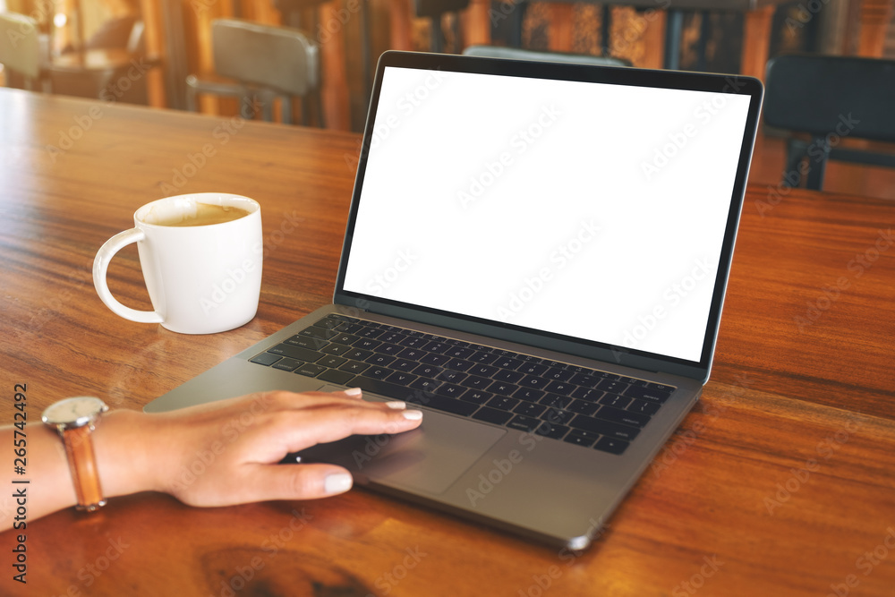 Mockup image of a woman's hand using and touching on laptop touchpad with blank white desktop screen with coffee cup on wooden table Mockup image of a woman's hand using and touching on laptop touchpad with blank white desktop screen with coffee cup on wooden table