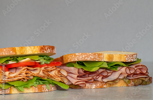 Freshly made deli style sandwich with lettus, several different kinds of vegetables, tomatoes, cheese, meats similar to ham, chicken or turkey.