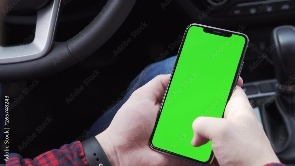 The guy is sitting in the car holding phone with green screen in his hands and scrolling through pages to the right and left up and down watching the news leafing through Instagram The guy is sitting in the car holding phone with green screen in his hands and scrolling through pages to the right and left up and down watching the news leafing through Instagram