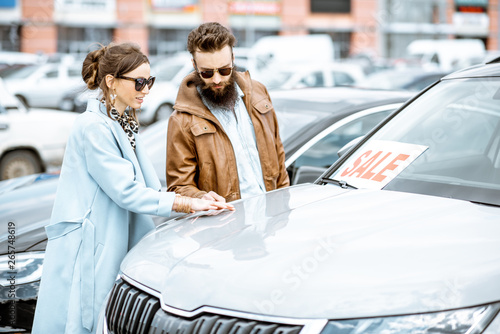 Young stylish couple choosing luxury car to buy on the open ground of the dealership