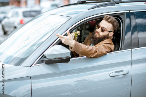 Stylish bearded man having a snack with tasty sandwich while driving a car in the city © rh2010