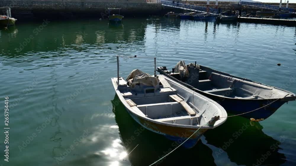 tilting shot of two old small fishing boats anchored in port on Persian gulf two old small fishing boats floating on limpid ocean water anchored in dock under direct natural sunlight tilting shot of two old small fishing boats anchored in port on Persian gulf two old small fishing boats floating on limpid ocean water anchored in dock under direct natural sunlight