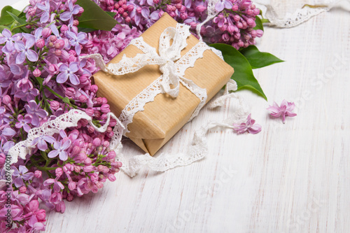 Lilac flowers and gift box on white wooden background  copy space