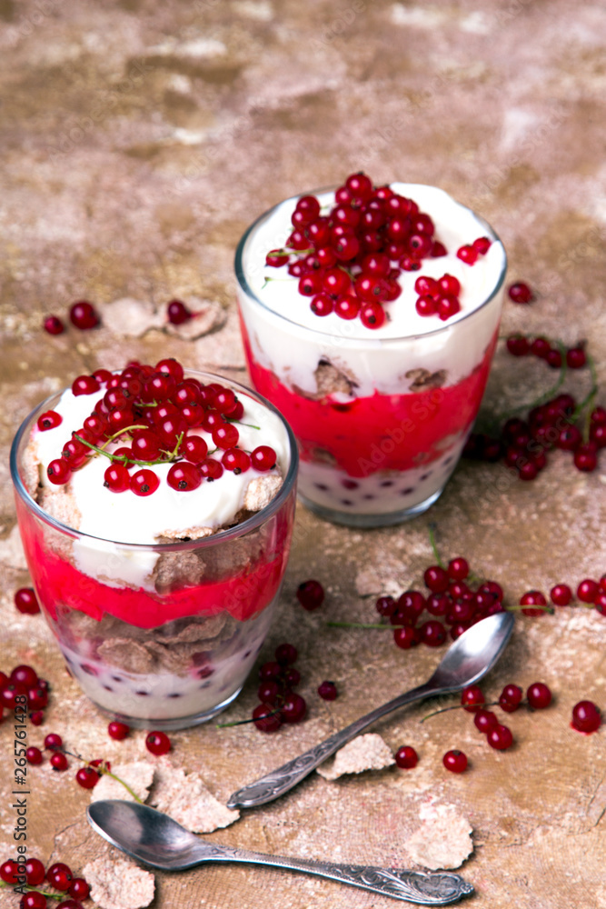 Healthy dessert with organic red currants, fresh yogurt and corn flakes. Dietary breakfast on a brown background