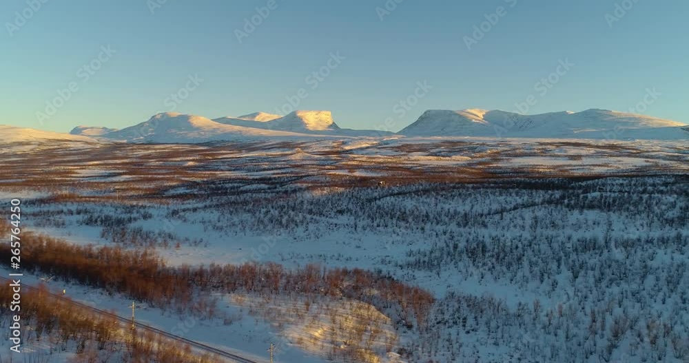 Lapporten sunset, C4k aerial, rising, drone shot, towards the lapponian mountains, near Abisko national park, at sundown, golden hour, on a sunny winter evening, Kiruna, Lapland, Norrbotten, in Sweden
