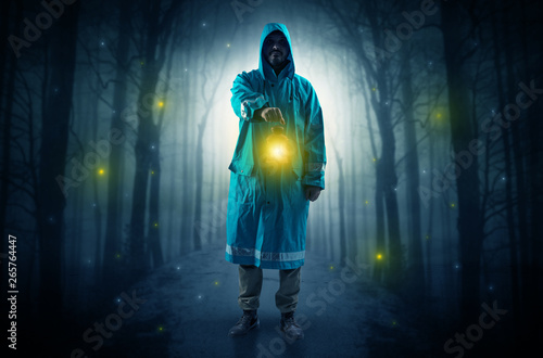 Man in raincoat coming from dark forest with glowing lantern in his hand concept 