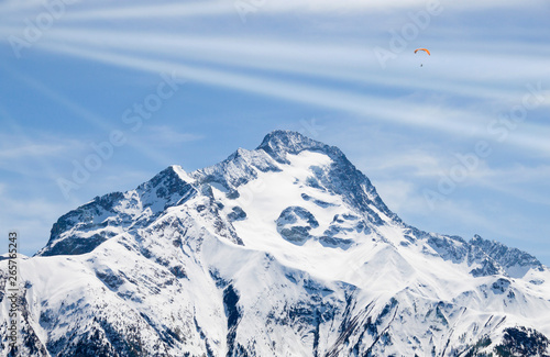two parachutes flying with rays of sun in the sky over a snowed mountain