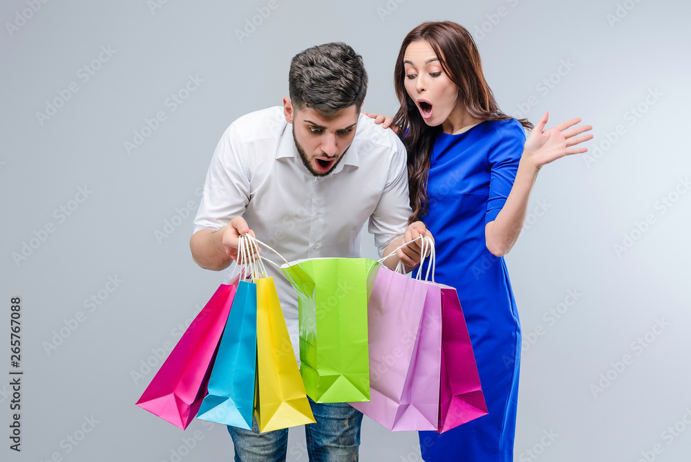 Attractive young couple with shopping bags from mall isolated over grey background. Girl shops with boyfriend on black friday sales Attractive young couple with shopping bags from mall isolated over grey background. Girl shops with boyfriend on black friday sales