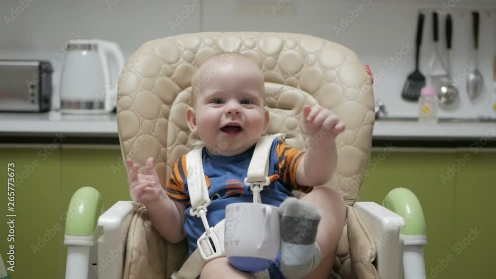 Baby sitting in a highchair and playing with a mug on a green kitchen Baby sitting in a highchair and playing with a mug on a green kitchen