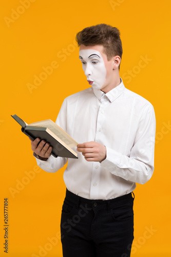 portrait of mime man artist reading book isolated on yellow background