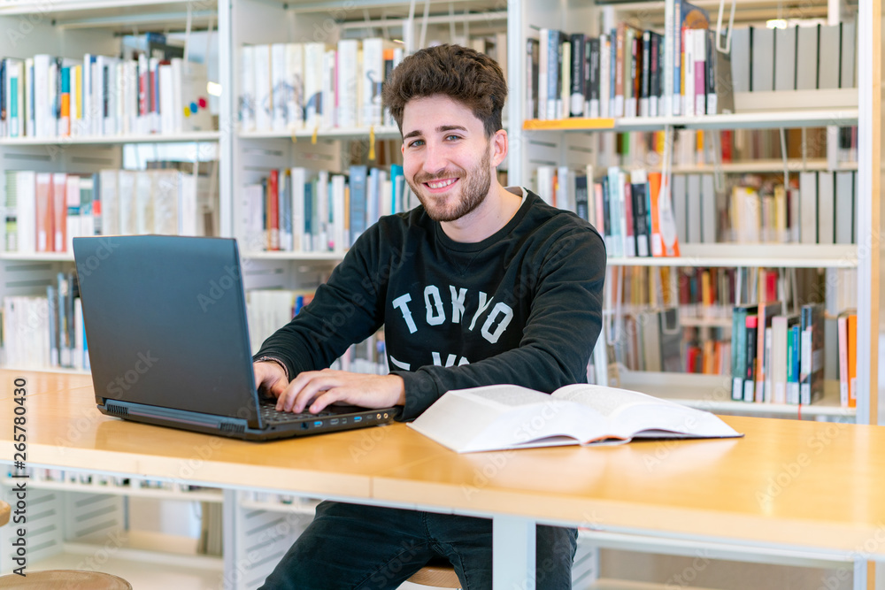 Young student sitting in front of the computer with books at the table happy smiling in the library Young student sitting in front of the computer with books at the table happy smiling in the library