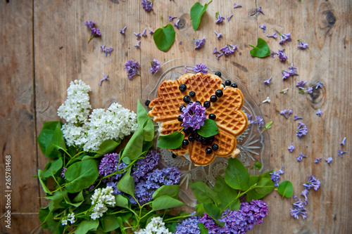 Homemade waffles with aronia, eggs and lilac flowers on the wooden table photo