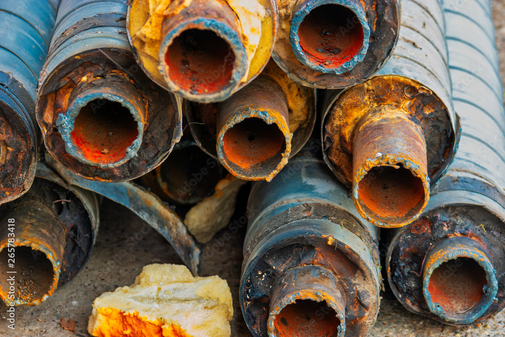 Water Pipeline repair. Large rusty steel pipe with insulation on the construction site in a plastic tube wrapper lying on the yard a bunch horizontally. Rusty old pipeline stacked up