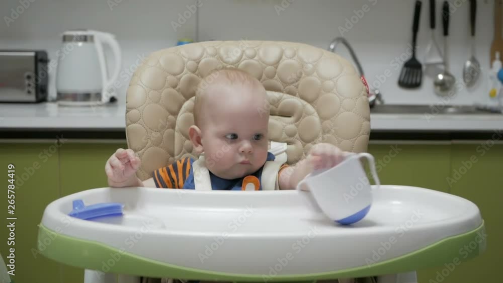 Baby sitting in a highchair and playing with a mug on a green kitchen Baby sitting in a highchair and playing with a mug on a green kitchen