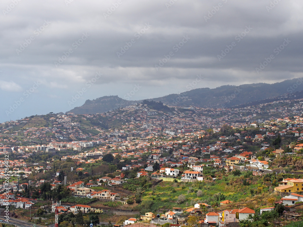 aerial cityscape view of the outskirts of funchal in Madeira with farms and houses with mountains and cloudy sky in the distance