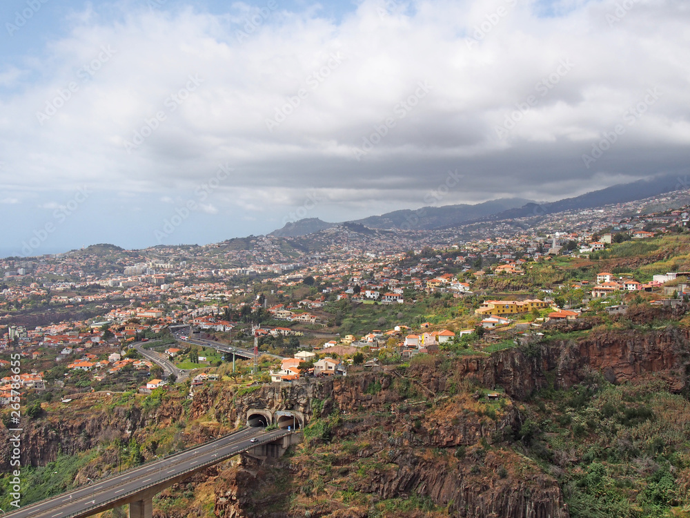 an aerial landscape view of the motorway bridge in funchal entering a tunnel in the valley with buildings and streets of the city