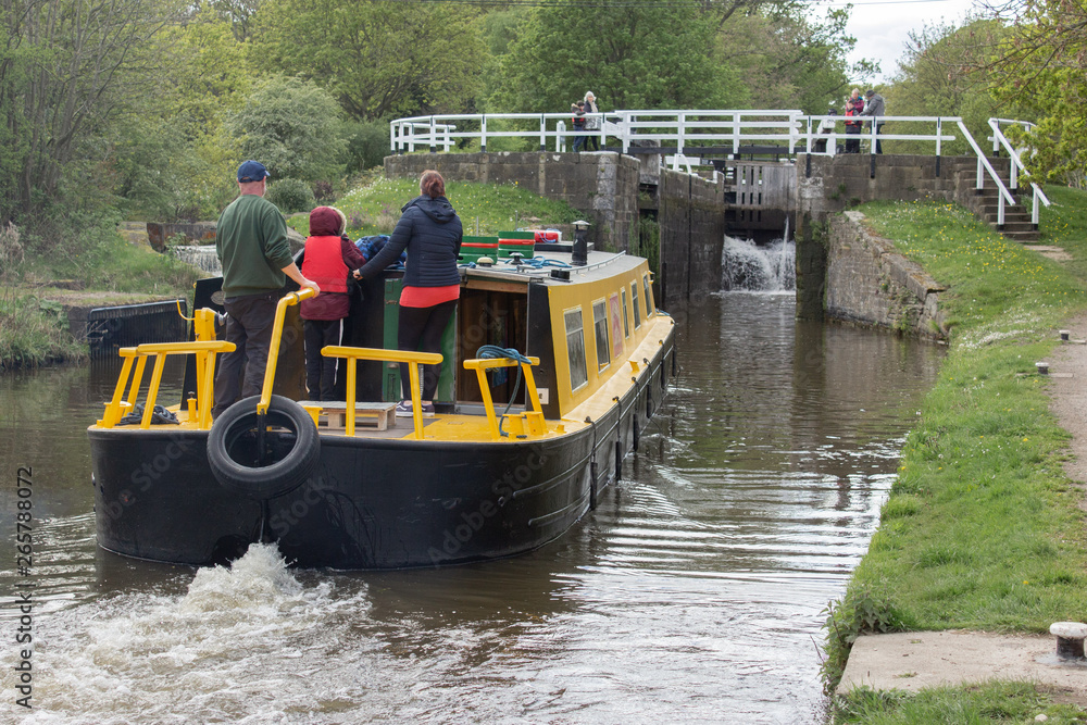 A family steers their boat towards the lock at Hirst Wood watched by bystanders A family steers their boat towards the lock at Hirst Wood watched by bystanders